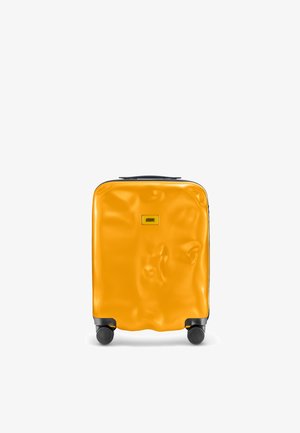 Valigia gialla rigida con superficie texturizzata, quattro ruote nere e una maniglia superiore per un facile trasporto. Dettaglio della cerniera nera e logo.