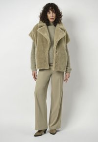 Faux fur, oversized khaki jasje met een grote kraag, knopen aan de voorkant en een zachte textuur, gecombineerd met een licht sweater en wijde broek.