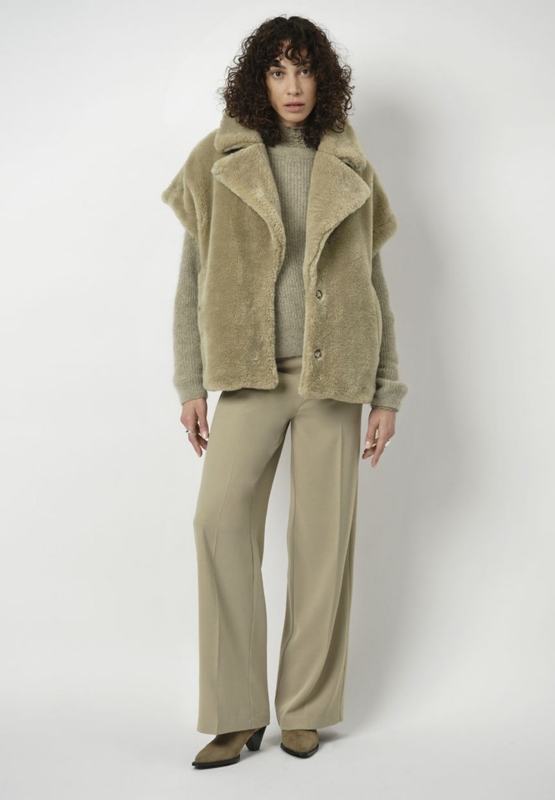 Faux fur, oversized khaki jasje met een grote kraag, knopen aan de voorkant en een zachte textuur, gecombineerd met een licht sweater en wijde broek.