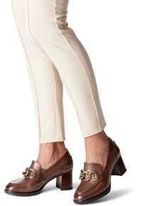 Scarpe con tacco in pelle marrone con dettaglio a catena, punta quadrata e tacco a blocco. Indossate con pantaloni attillati color crema.