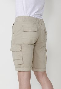 Pantaloni scurți cargo bej cu un tiv elastic, multiple buzunare laterale și tiv pliat. Realizați dintr-un material ușor, cu o textură netedă.