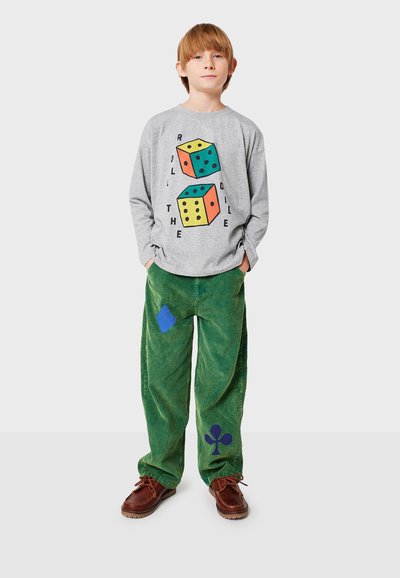 Camisa de manga larga gris con un gráfico de dados coloridos. Pantalones de pana verde con parches azules. Zapatos marrones completan el conjunto.