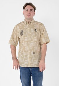Camicia a maniche corte in tessuto beige con un motivo testurizzato, dotata di logo, bottoni e dettagli grafici in tonalità più scure.