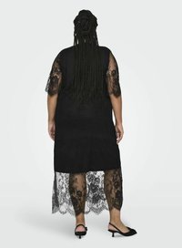 Abito lungo nero con maniche corte in pizzo e orlo trasparente in pizzo. L'abito presenta una texture liscia con dettagli in pizzo intricati nella parte inferiore.