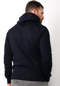 Sudadera con capucha azul marino hecha de un tejido suave. Cuenta con una gran capucha y puños acanalados. Diseño simple sin patrones ni gráficos visibles.