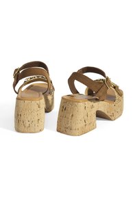 Braune Wildleder-Plateausandalen mit Korkabsatz, ausgestattet mit zwei verstellbaren Riemen und einer goldenen Schnalle sowie einem strukturierten Fußbett.