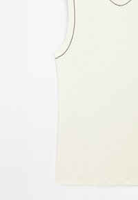 Ærmeløs creme top i blød stof med V-hals og kontrasterende tynde sorte syninger langs kanterne. Enkelt design uden mønstre.