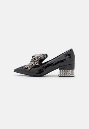 Chaussure noire à talon bas effet crocodile, talon bloc clouté argenté et grand nœud argenté perlé sur le dessus.