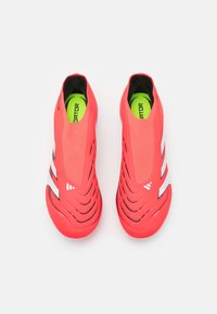 Světlé červené sportovní boty se štíhlým, aerodynamickým designem. Texturovaný svršek s výřezy a bílými akcenty. Živé zelené stélky.