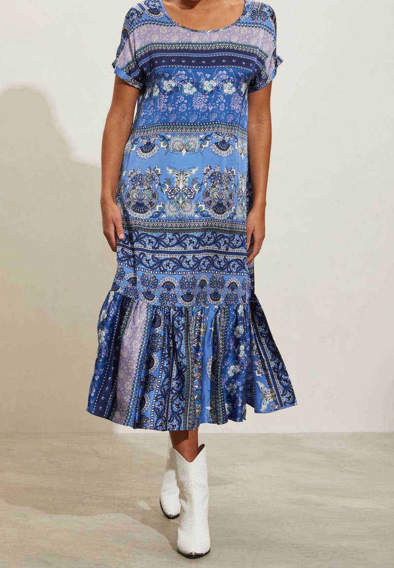 Modré šaty s potiskem a krátkým rukávem, zdobené květinovými a paisley vzory. Rozšířený lem s texturovaným dolním okrajem. Nosené s bílými kovbojskými botami.