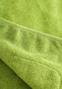 Zöld törölköző, puha frottír anyagból készült, sima szegéllyel és egy texturált felülettel, amelyen hurkos szálak találhatók a jó nedvszívás érdekében.