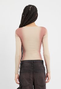 Langermet topp med et gradientdesign som går fra beige til lys rosa. Glatt tekstur; tettsittende silhuett. Kombinert med mørke cargo-bukser.