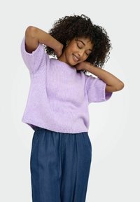 Cimdi ar īsām piedurknēm, gaiši violetas adītas vilnas džemperis ar ribota faktūru un brīvu piegriezumu, apvienots ar tumši zilām džinsiem.