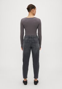 Siva rebrasta majica z dolgimi rokavi v kombinaciji z visokim pasom in ožjimi temno sivo ženski jeans hlačami. Stranske in zadnje žepe so vidni, gladka tekstura tkanine.