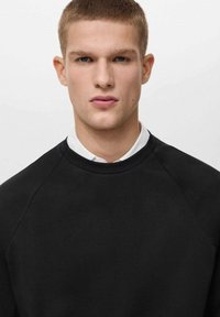 Felpa nera con collo a giro e maniche raglan, realizzata in tessuto liscio, presenta un design minimal con un collo pulito e senza grafiche.