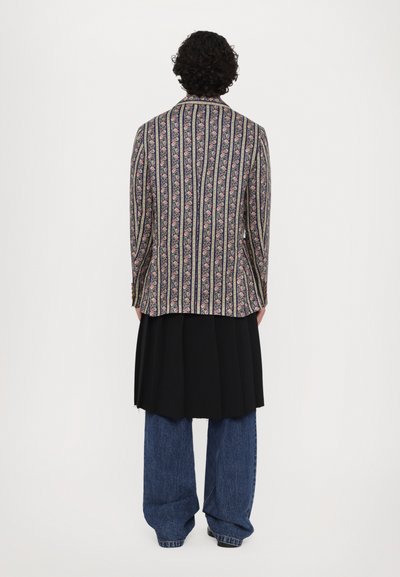 Floral-patterned blazer with vertical stripes in dark colors, paired with a black pleated skirt and loose blue denim jeans.