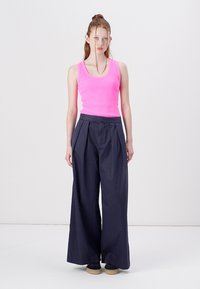 Fuchsia geripptes Tanktop kombiniert mit weiten marineblauen Hosen, die Falten und eine hohe Taille haben. Minimalistisches Design, klare Linien und glatte Textur.