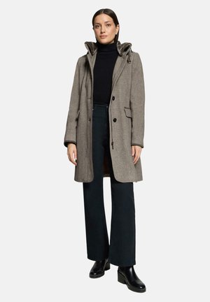 Woman wearing a gray hooded coat over a black turtleneck, black wide-leg pants, and black ankle boots, standing against a plain background.