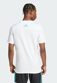 Camiseta blanca de manga corta hecha de algodón, con un logo de Adidas en azul claro en la parte superior de la espalda, textura suave y corte clásico.