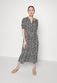Vestido de estampado de leopardo em preto e branco com mangas curtas em balão, decote em v e uma saia fluída. Usado com sapatos slip-on de trama em tom bege.