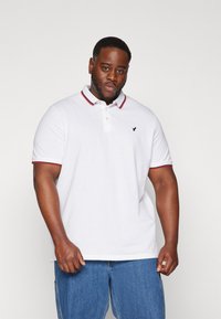 White polo shirt with red and blue collar and sleeve accents, featuring a small black logo on the chest. Made from textured cotton fabric.