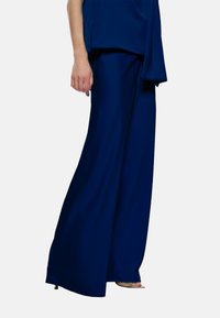 Pantaloni larghi navali in un tessuto liscio, con una caduta elegante e un design a vita alta. Abbinati a una maglia coordinata.