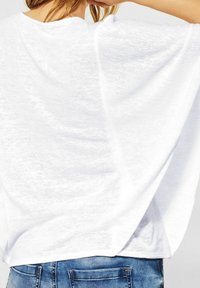 Vit löst sittande skjorta med en mjuk, texturerad yta och sänkta axlar, som är ihop med blå denimjeans.