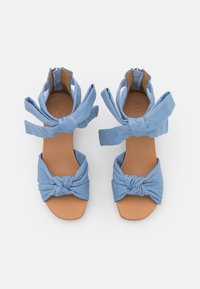 Modré látkové sandály s uzlíkovým předním dílem a vázáním kolem kotníku, s hnědou stélkou a hladkým povrchem, nabízející otevřenou špičku.