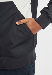Black and white sweatshirt with a hood, featuring a kangaroo pocket, ribbed cuffs, and a textured finish at the hem.
