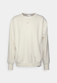 Cremefarvet sweatshirt lavet af blødt stof, med rund halsudskæring, lange ærmer, ribbede manchetter, og et diskrét Nike-logo på brystet.