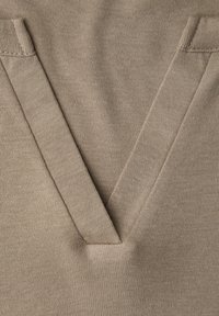 Nahaufnahme eines beigen Strickstoffs mit V-förmigem Ausschnitt und verstärkter Naht an beiden Seiten.