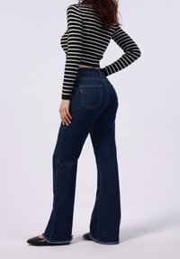 Vaqueros acampanados de cintura alta en denim azul oscuro con un dobladillo deshilachado. Combinados con un top corto a rayas en blanco y negro.