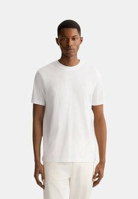 T-shirt bianca in cotone con collo rotondo, maniche corte e un logo discreto sul petto. Tessuto liscio, design a taglio dritto.