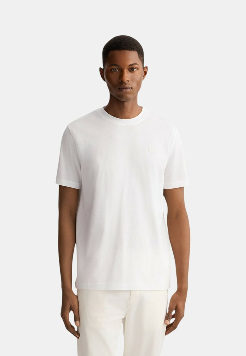 T-shirt bianca in cotone con collo rotondo, maniche corte e un logo discreto sul petto. Tessuto liscio, design a taglio dritto.