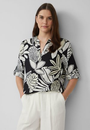 Zwart-wit korte mouwen shirt met een bloemenpatroon, voorzien van een V-hals en zachte stof. Gecombineerd met witte, lichte broeken.