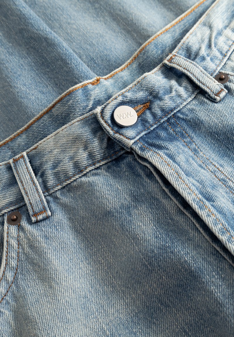 Hellblaue Jeans aus Denim mit klassischem Fünf-Taschen-Design. Verfügt über einen silbernen Knopfverschluss und kontrastierende orangefarbene Nähte.
