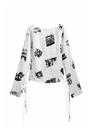 White long-sleeve top with black graphic prints, featuring a round neckline and tie closures at the sleeves, made from textured fabric.