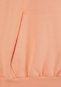 Sudadera de color melocotón, mezcla de algodón suave, con un bolsillo delantero, dobladillo acanalado y detalle fruncido en la cintura. Textura suave.
