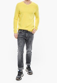 Maglione giallo a scollo a V, jeans grigi slim-fit con una finitura sbiadita e sneaker nere con dettagli blu. L'outfit ha un aspetto casual.