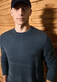 Navy blue knit sweater featuring horizontal striped texture with varying patterns. Crew neck style with long sleeves.