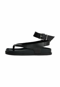 Sandalo in pelle nera con design aperto sulla punta, cinturino alla caviglia con fibbia e suola piatta spessa. Texture liscia e silhouette minimalista.