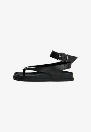 Sandal de cuero negro con diseño de punta abierta, tira en el tobillo con hebilla y una suela plana gruesa. Textura suave y silueta minimalista.