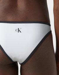 Bikini blanc avec des finitions noires, arborant un petit logo "cK" noir à l'arrière. Texture lisse, design minimaliste.