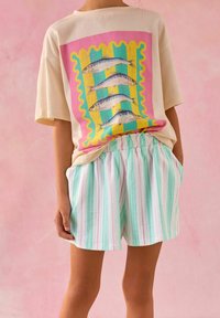 T-shirt beige oversize avec motif de poisson en rose, vert et jaune ; short rayé pastel en vert menthe, rose et blanc ; taille élastique.