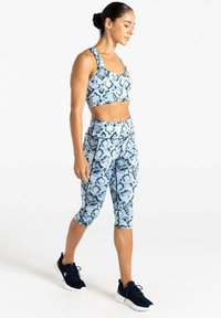 Sostenedor deportivo con estampado de serpiente en azul y blanco y leggings capri, silueta ajustada, material elástico, combinados con zapatillas deportivas negras.