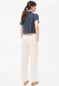 Przycięta granatowa koszula w białe paski, krótki rękaw i kołnierzyk, dopasowana do luźnych, kremowych spodni. Proste sandały dopełniają strój.