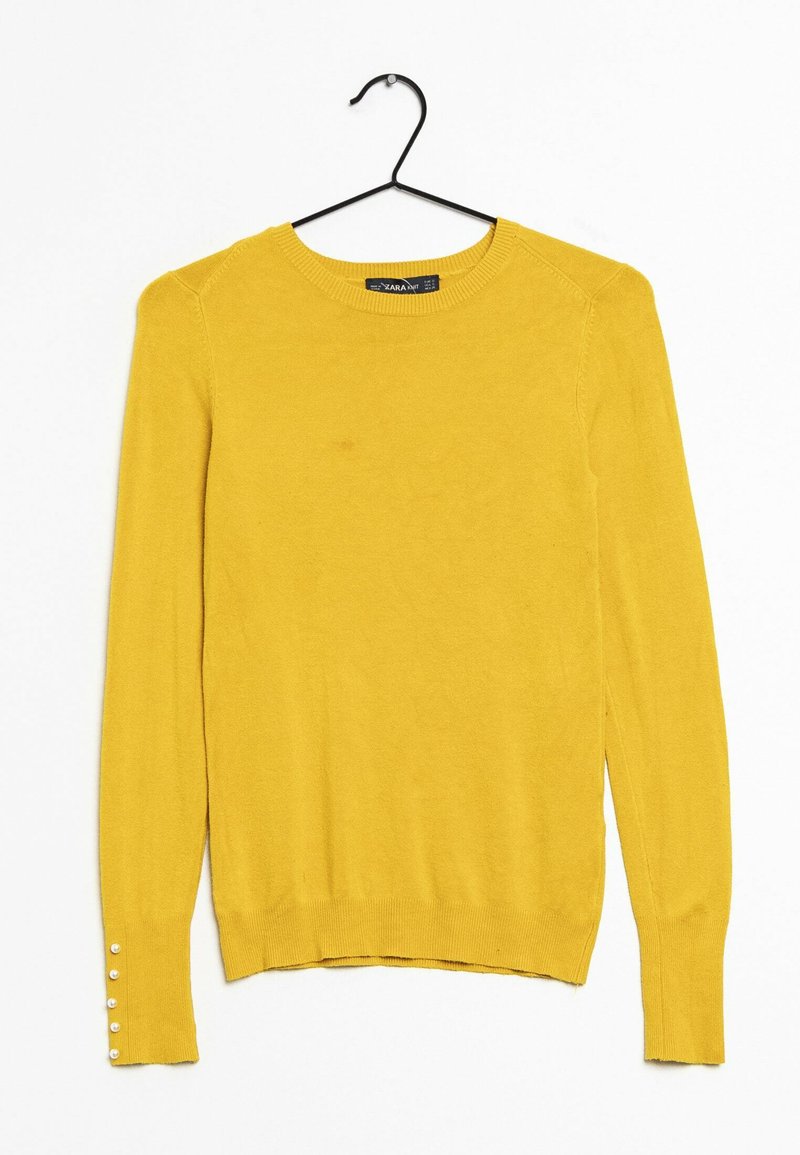 Gelber Strickpullover mit langen Ärmeln, rundem Ausschnitt und dekorativen Knöpfen an den Manschetten. Weiche Textur, minimalistisches Design.