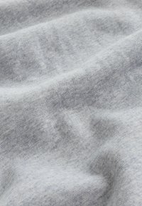 Meka, svijetlosiva tkanina s suptilnom tkanom teksturom i nježnim naborima, koja pokazuje fine detalje pletenja.