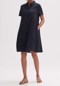 Mörkblå klänning med knappar, krage, korta ärmar och två sidofickor. Strukturerad tyg med en avslappnad, A-linjeformad silhuett.