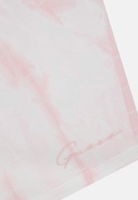 Tricou legat de tie-dye de culoare roz deschis, cu o textură netedă, având un logo subtil "Guess" în scris roz în partea stângă jos.